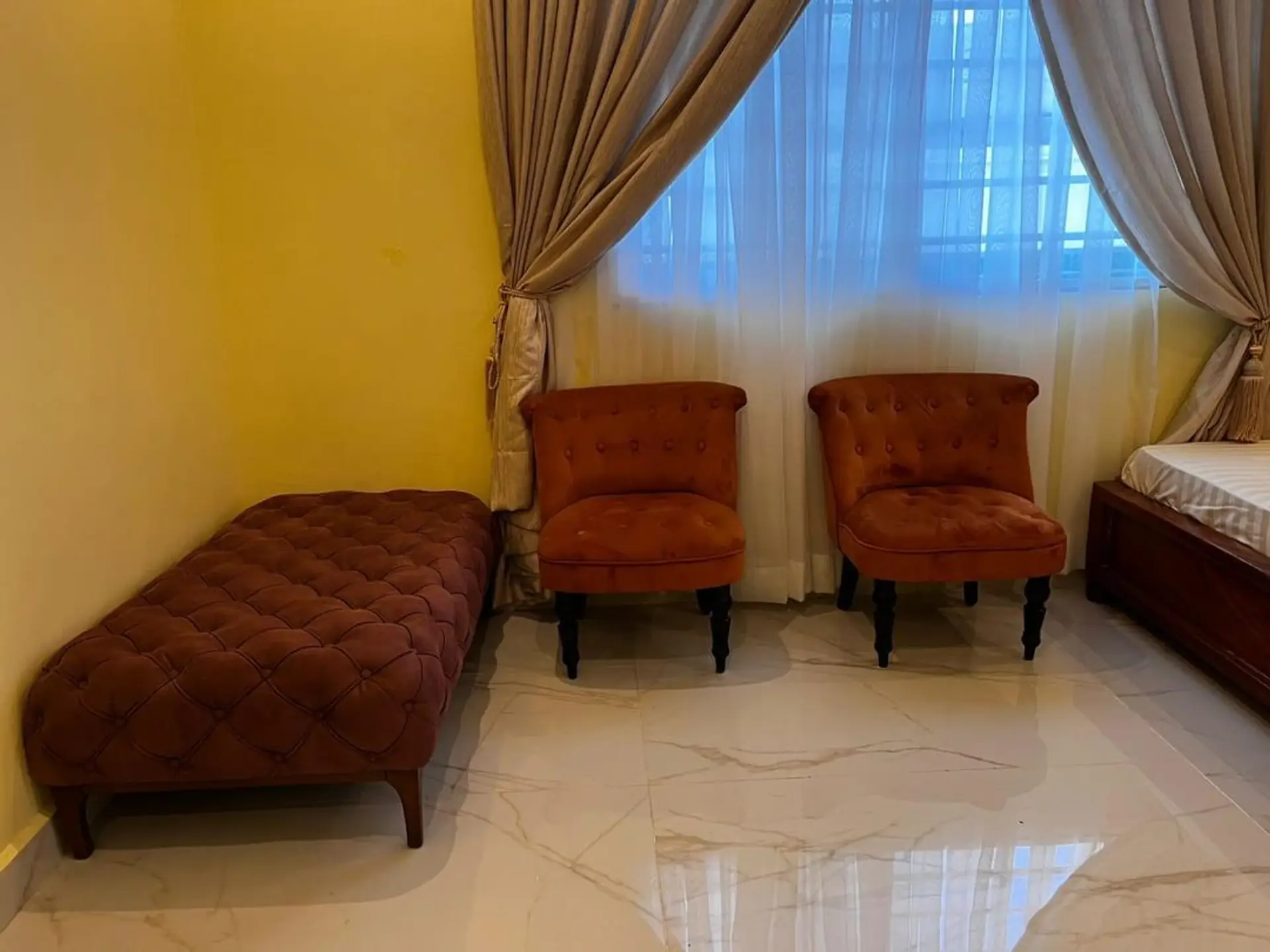 A velvet daybed and rust armchairs in a marble-floored bedroom suite