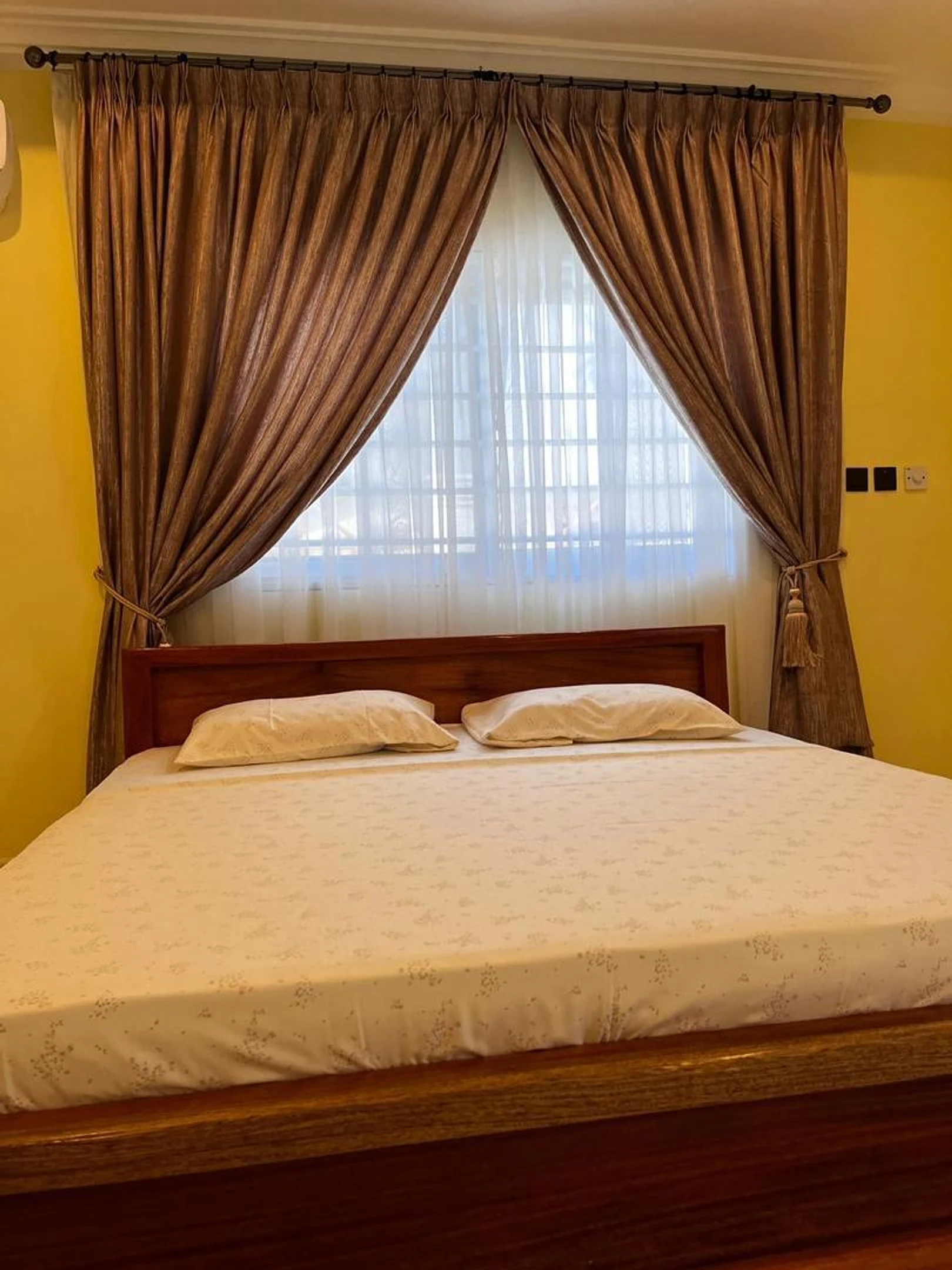 King bedroom with a wooden bed frame, layered curtains and soft light