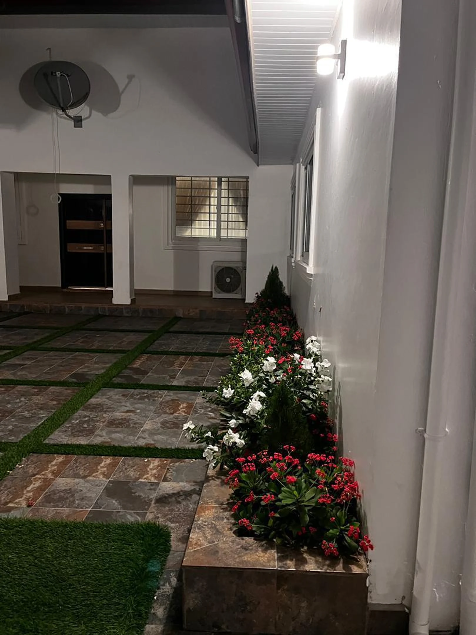Flower beds and lantern light along the villa wall at night